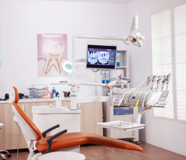 Dental chair and other accesorries used by dentist in empty cabinet. Stomatology cabinet with nobody in it and orange equipment for oral treatment.